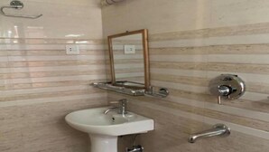 A bathroom with a pedestal sink, a mirror, a towel rack, and a towel dispenser. - MeroStay 141 Hotel RG (Kathmandu)