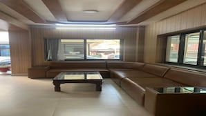 A modern living room with a sectional sofa, a glass-top coffee table, and large windows offering a view of the street. - MeroStay 141 Hotel RG (Kathmandu)