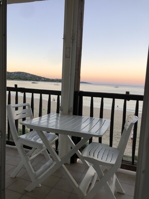 A balcony with a white table and chairs, overlooking a beach with a calm sea and distant hills. - MerSea Studio, on the beach, 2–4 people (PORT GRIMAUD)