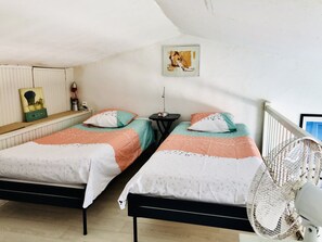 A bedroom with two beds, a bedside table, a lamp, a picture on the wall, and a standing fan. - MerSea Studio, on the beach, 2–4 people (PORT GRIMAUD)
