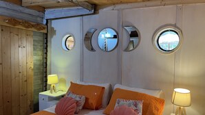 A bedroom with a wooden ceiling, a bed with orange bedding, multiple round mirrors on the wall, and a nightstand with a lamp. - Wild Wild Nest Sperlongaresort (Sperlonga)