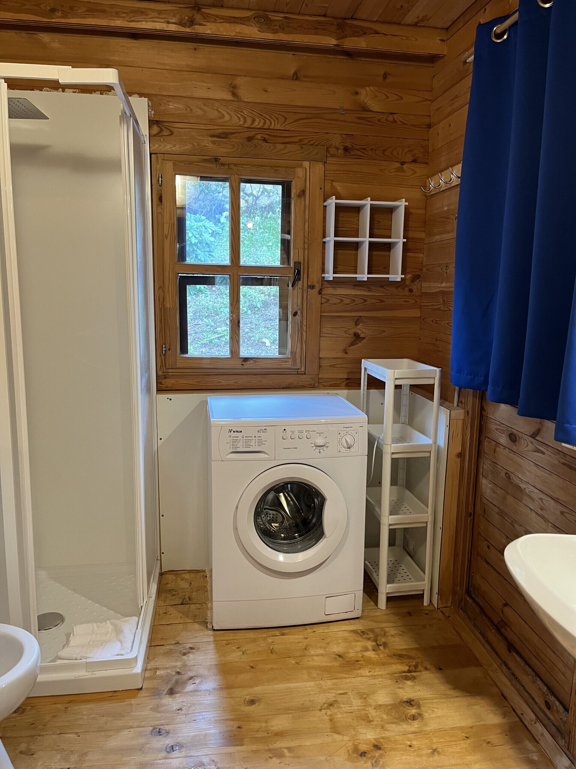 A compact bathroom with a washing machine, a shower, and a window.