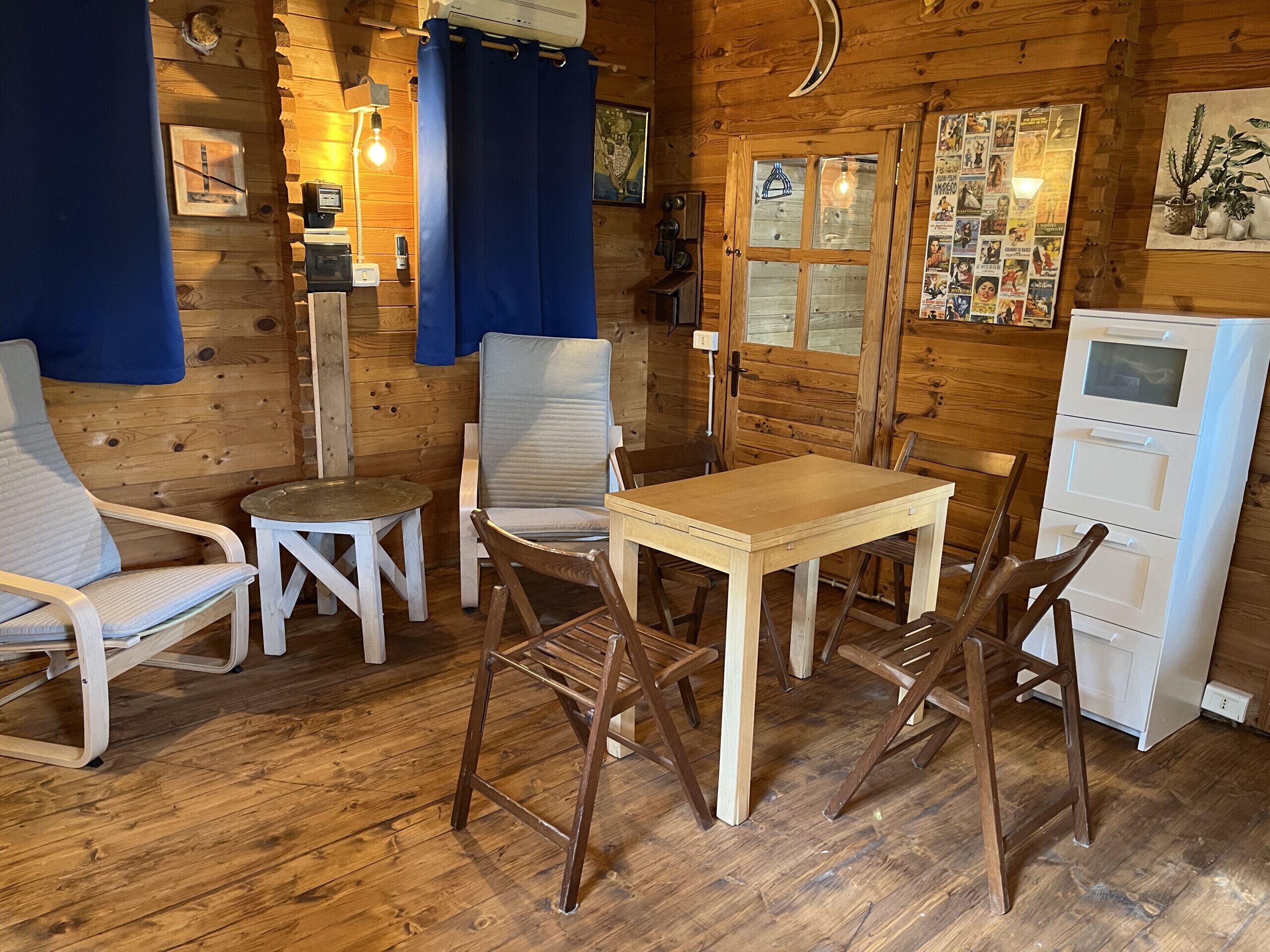 A cozy wooden cabin interior with a dining table, two chairs, a small round table, and a white cabinet.