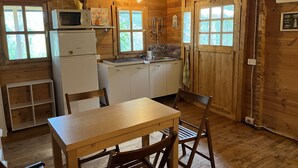 A wooden cabin interior with a dining table, chairs, a refrigerator, a microwave, a sink, and a window. - Wild Wild Nest Sperlongaresort (Sperlonga)