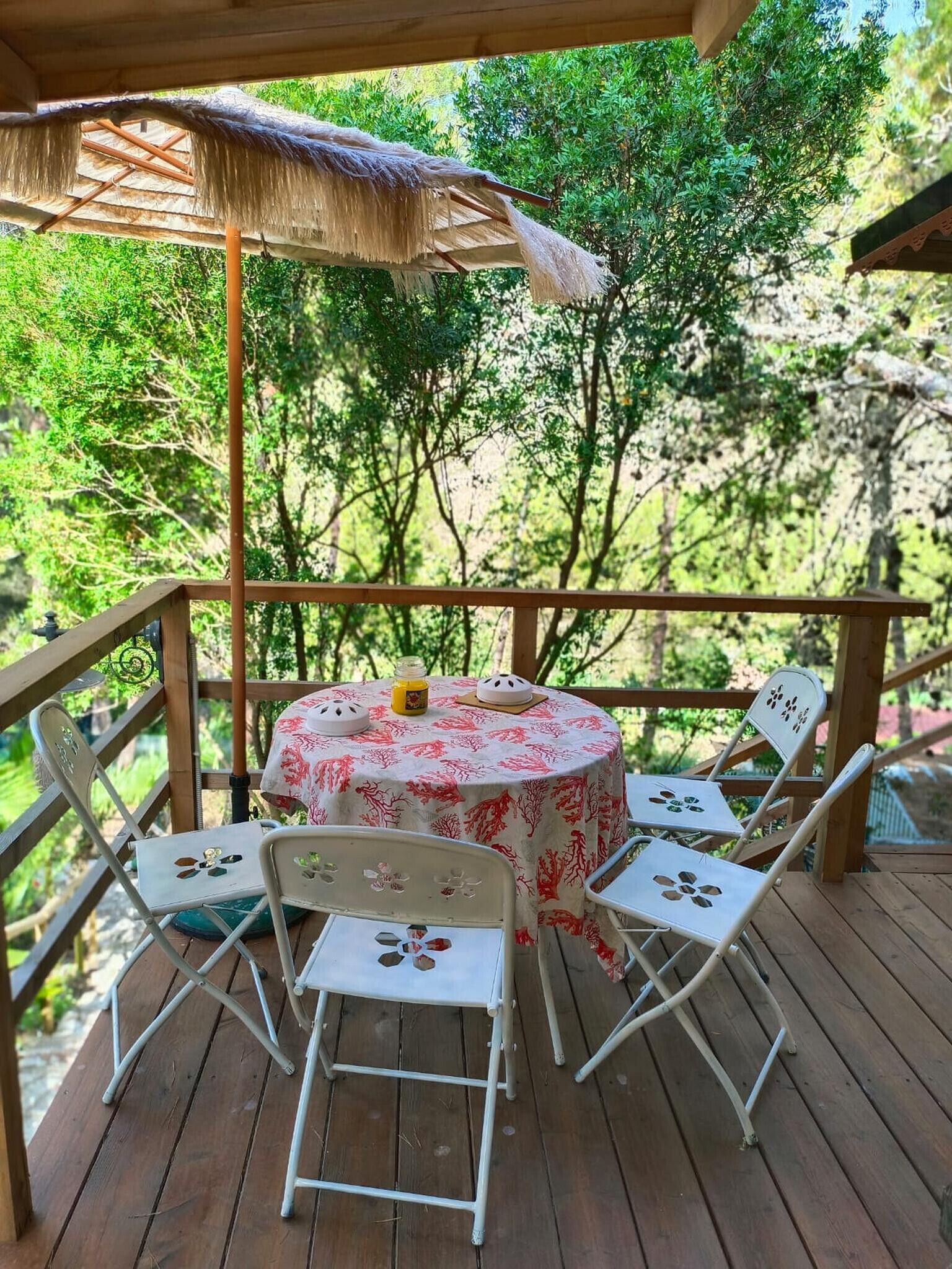 A wooden deck with a round table and four chairs, surrounded by a wooden railing, set against a backdrop of lush greenery.