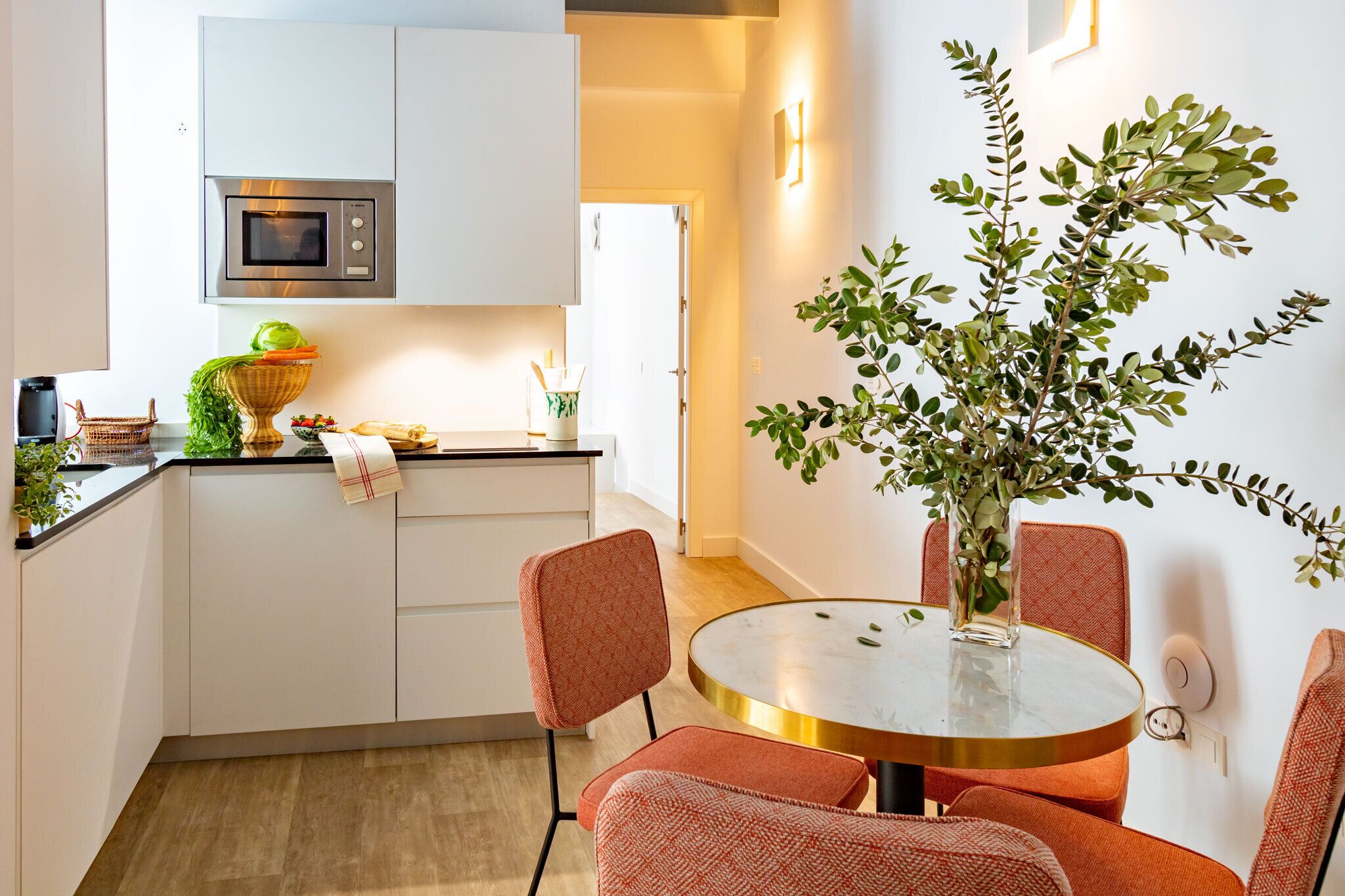 A modern kitchen with white cabinets, a microwave, and a dining area with a round table and orange chairs.