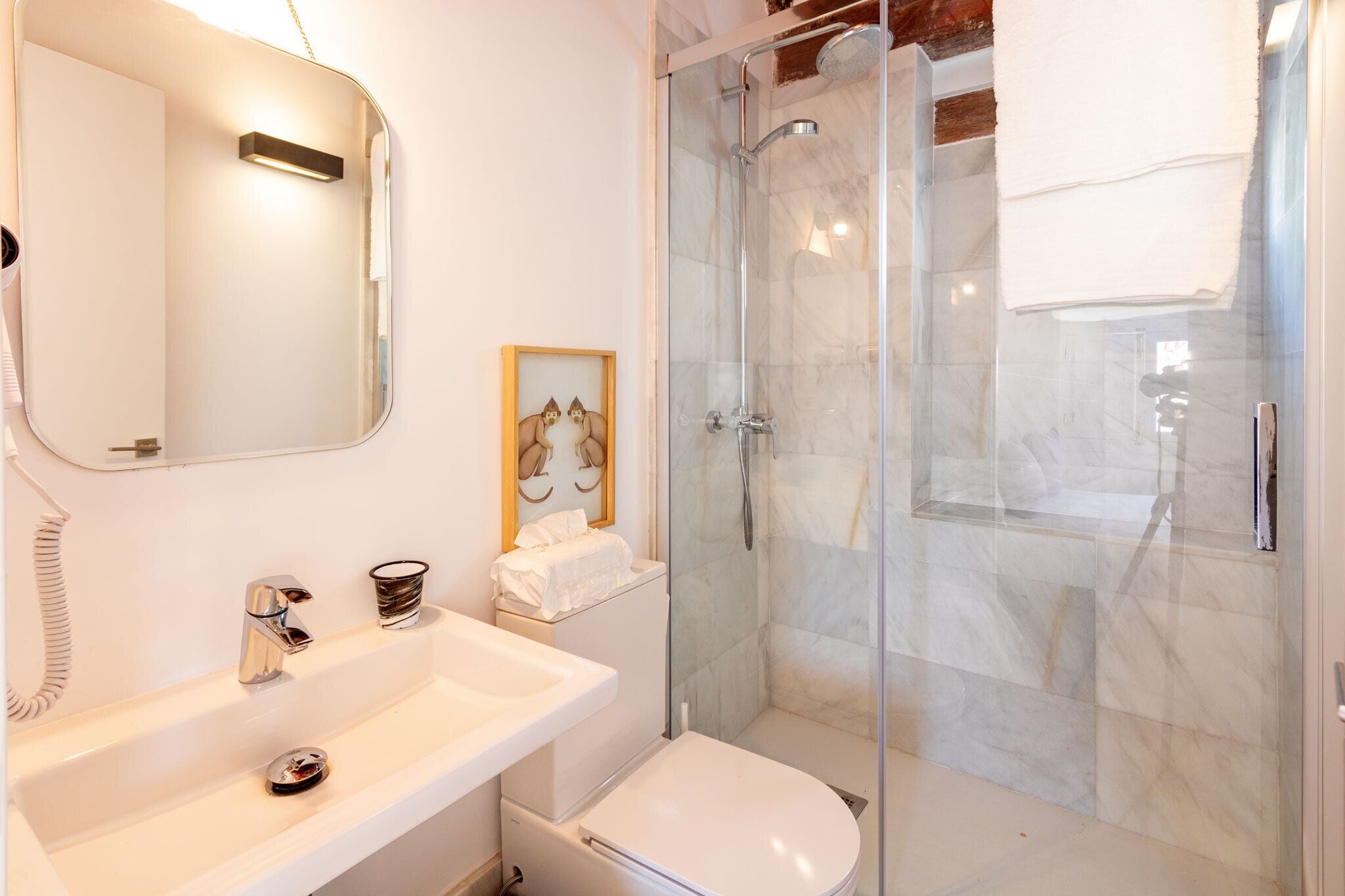 Een moderne badkamer met een douchecabine van glas, een witte wastafel en een toilet.