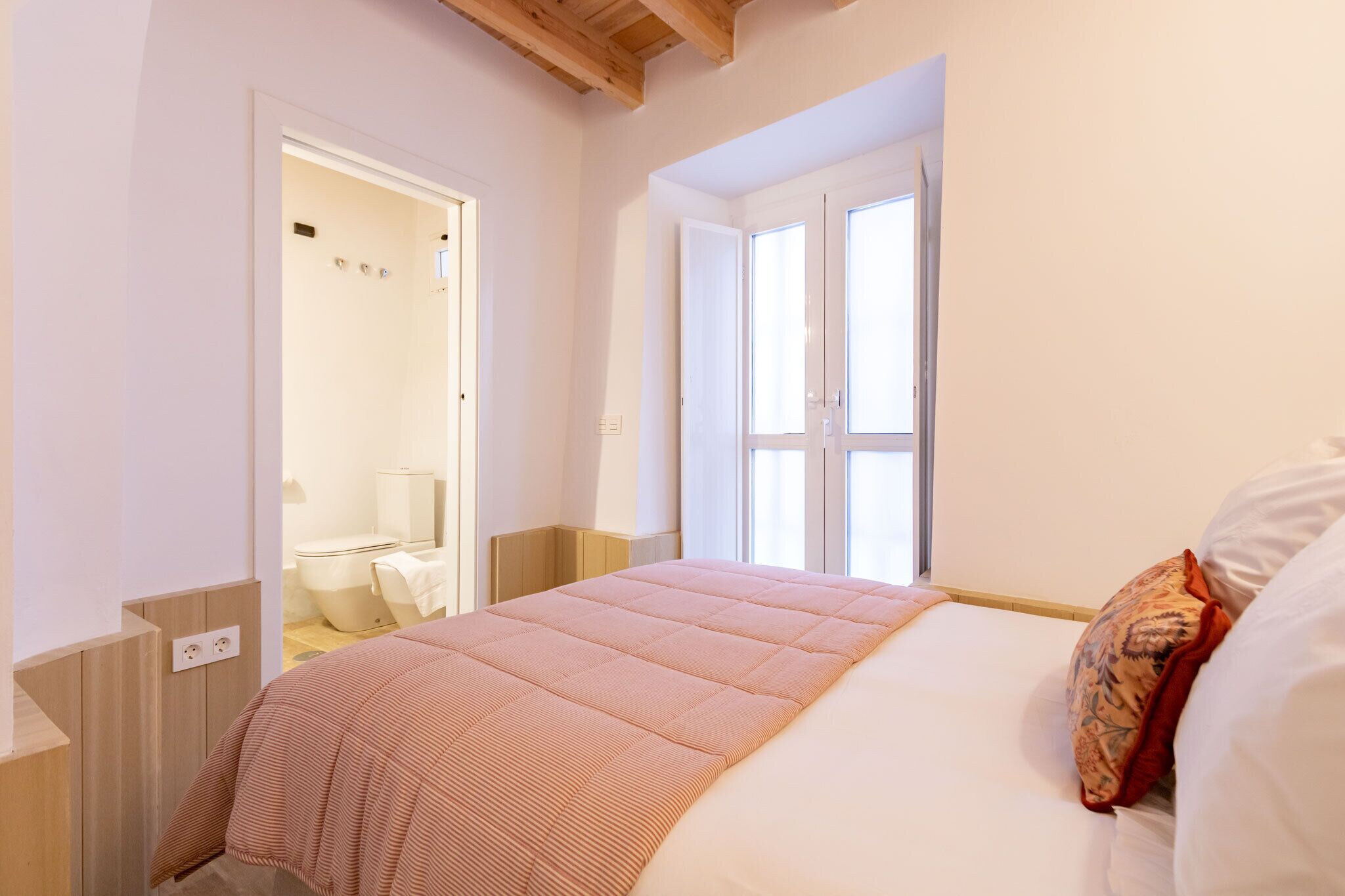A bedroom with a bed, a window, and a bathroom visible through an open door.