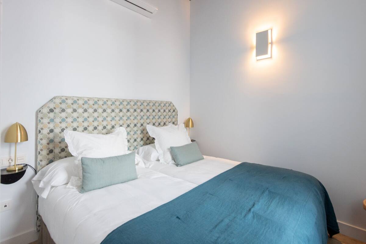 A neatly made bed with a patterned headboard, white bedding, and a blue throw blanket. There are two bedside lamps with gold bases.