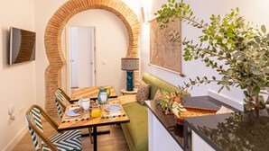 A dining area with a brick archway, a table set with plates, a pitcher, and a glass of orange juice. There is a green sofa and a plant on the right. - Pimienta 9 - Santa Cruz by Valcambre  (Seville)