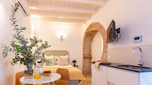 A compact hotel room with a bed, a small dining table with chairs, a kitchen area with a sink, and a large window. - Pimienta 9 - Santa Cruz by Valcambre  (Seville)