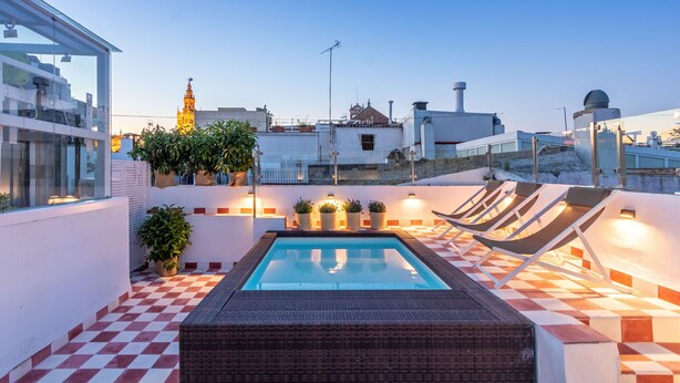 A rooftop pool area with a checkered floor, lounge chairs, and potted plants. - Pimienta 9 - Santa Cruz by Valcambre  (Seville)