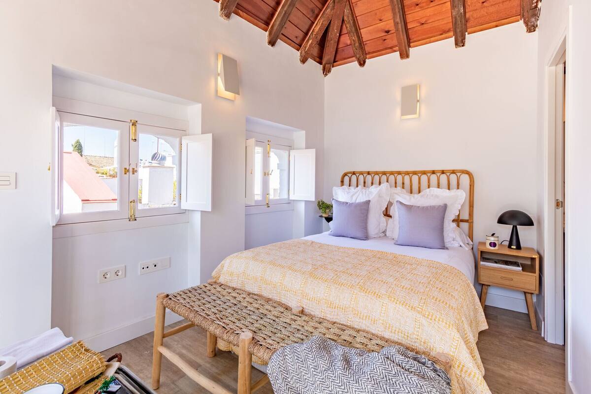 A bedroom with a bed, bench, bedside table, and a window with an open door.
