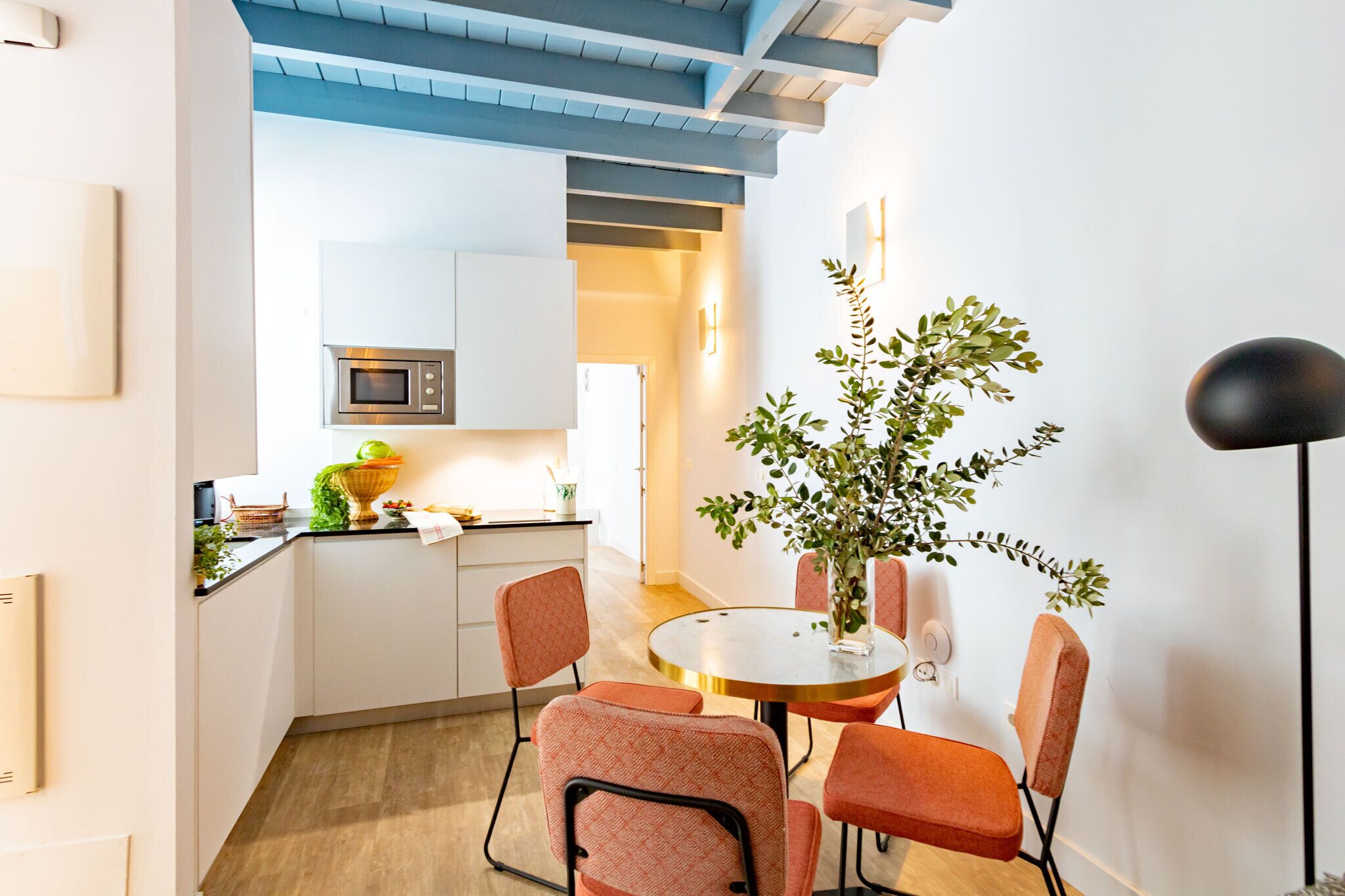 Una cocina moderna con armarios blancos, un microondas y un comedor con una mesa redonda y sillas naranjas.