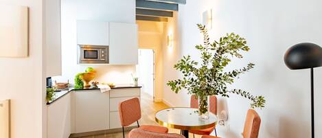 Una cocina moderna con armarios blancos, un microondas y un comedor con una mesa redonda y sillas naranjas.