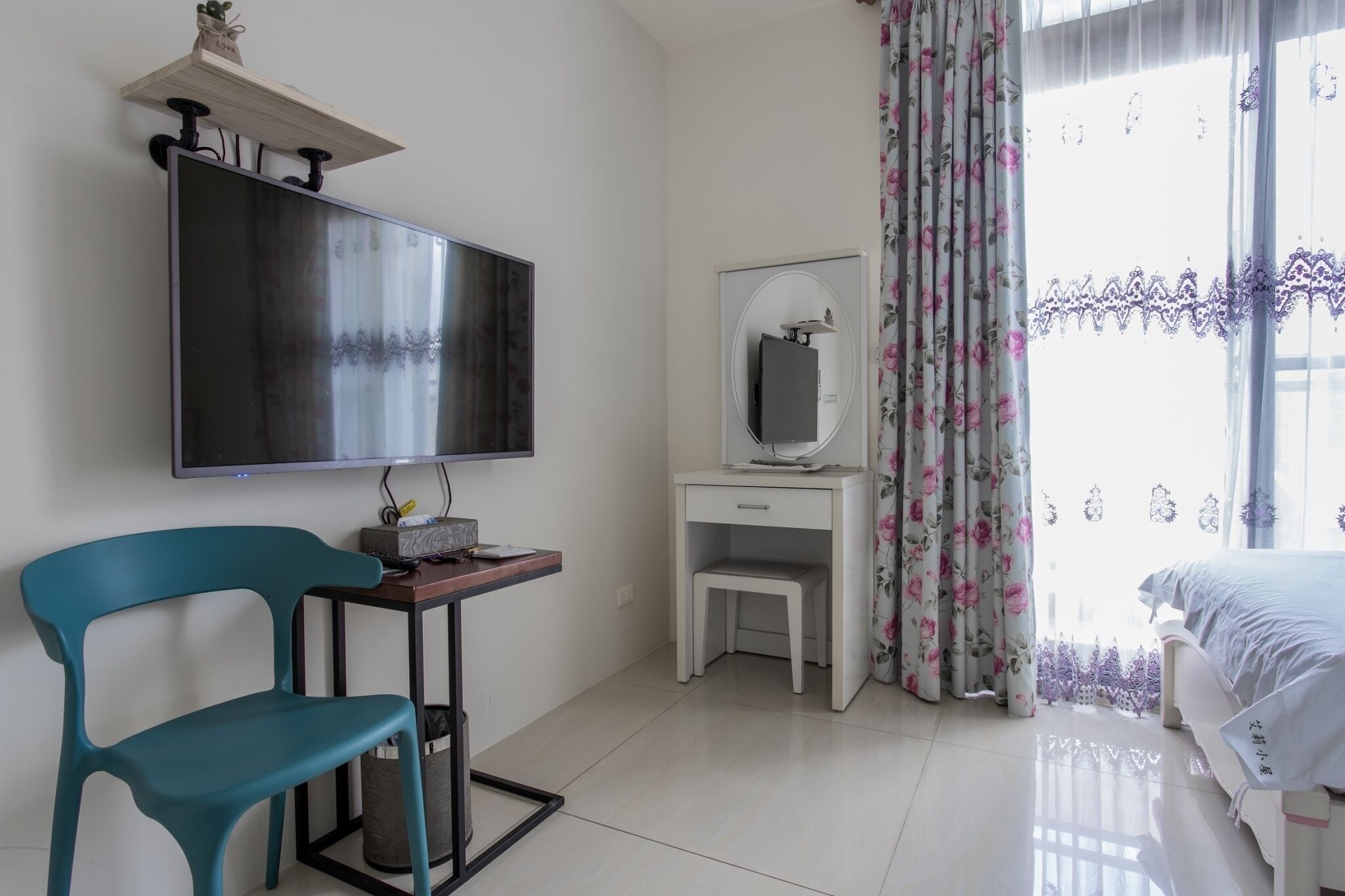 Une chambre à coucher comprenant un lit, un bureau avec une chaise, une télévision, une commode et une fenêtre avec des rideaux.