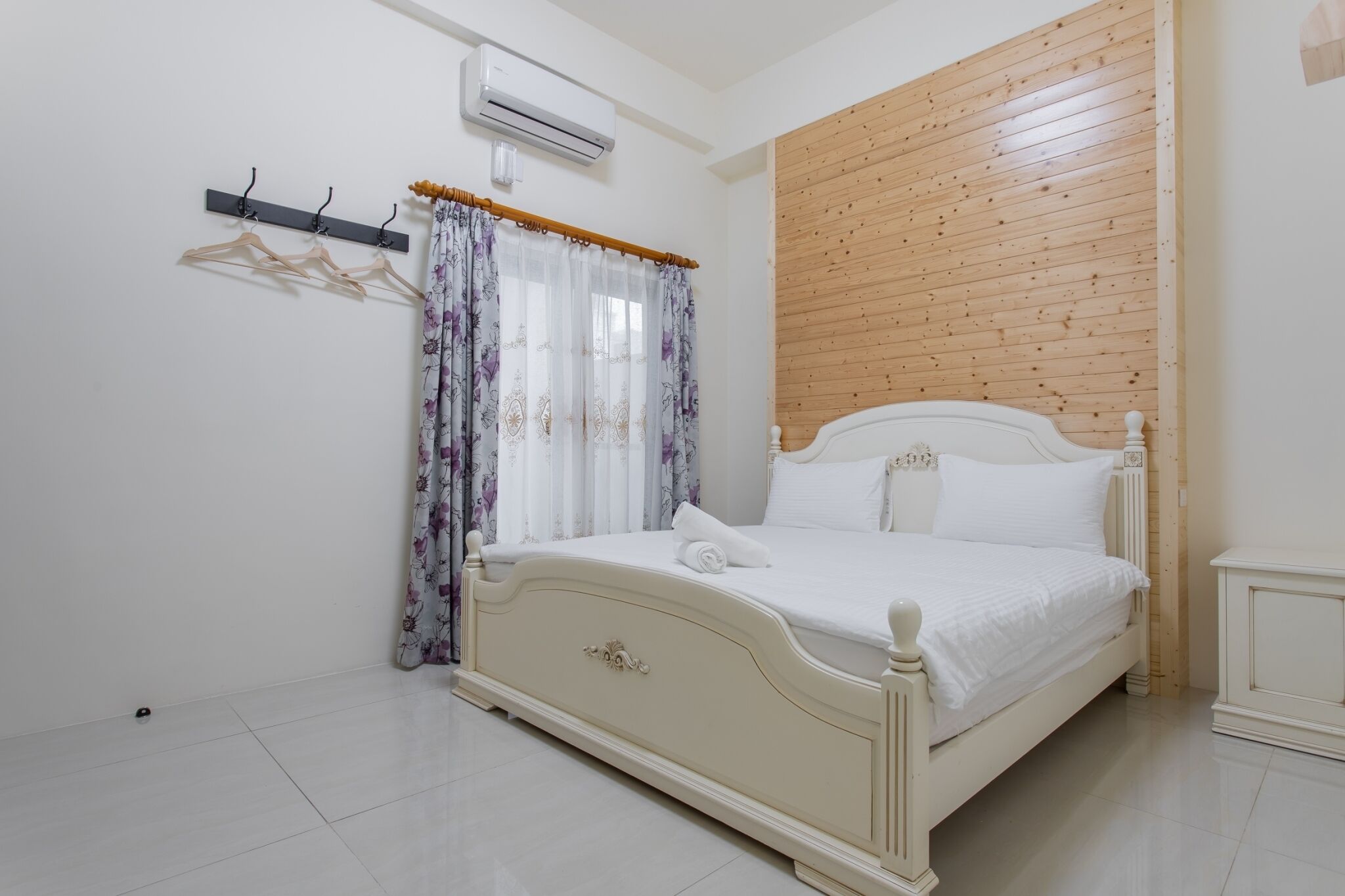 Ein ordentlich eingerichtetes Schlafzimmer mit einem Bett, einer Klimaanlage, einer Wand aus Holzpaneelen und einem Kleiderhaken mit Kleiderbügeln.