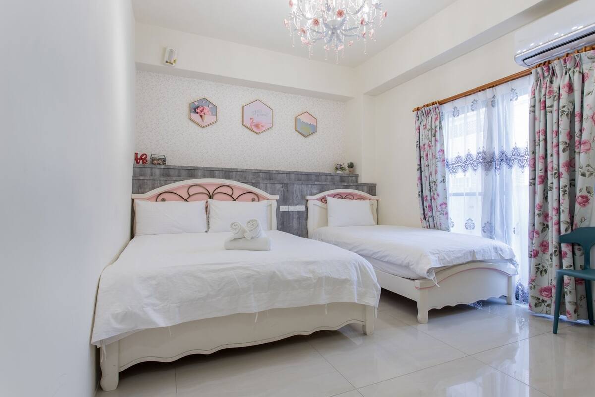 Une chambre avec deux lits, un lustre, une fenêtre ornée de rideaux à motifs floraux et un mur décoré de motifs hexagonaux.