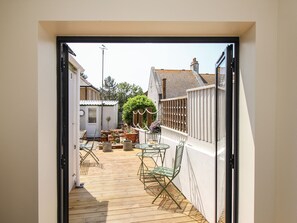 A narrow outdoor patio with a wooden floor, metal chairs, a small table, and potted plants. - Blanche Cottage (Weymouth)