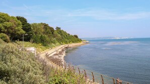 A coastal landscape with a wooden walkway along the shore, a clear sky, and distant mountains. - Blanche Cottage (Weymouth)