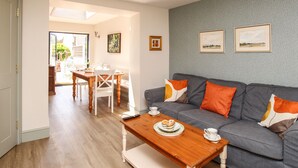 A living room with a grey sofa, wooden coffee table, and a dining area with a table and chairs. - Blanche Cottage (Weymouth)
