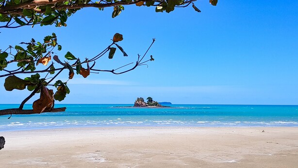 A beach with clear blue water, a sandy shore, and a small island with vegetation in the distance.