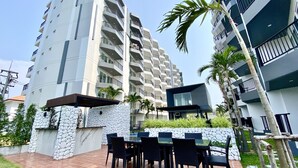 A modern apartment building with multiple balconies, a patio area with outdoor furniture, and a stone wall.