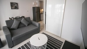 A modern living room with a grey sofa, a small round table, and a kitchen in the background.