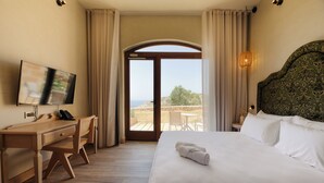 Habitación de hotel con cama, escritorio, silla, televisor y vistas a través de un ventanal.