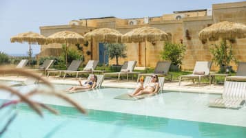 Una piscina al aire libre, sombrillas, sillones reclinables de piscina