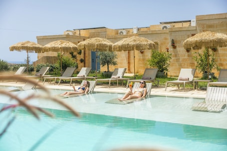 Una piscina al aire libre, sombrillas, sillones reclinables de piscina