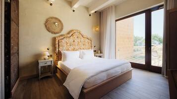 A bedroom with a large bed, a nightstand with a lamp, a decorative wall hanging, and a view through a sliding door to an outdoor area.