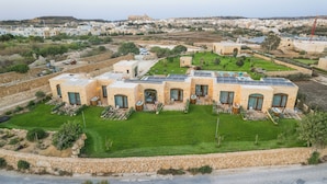 Una villa moderna con un patio amplio, paneles solares y vistas del pueblo circundante.