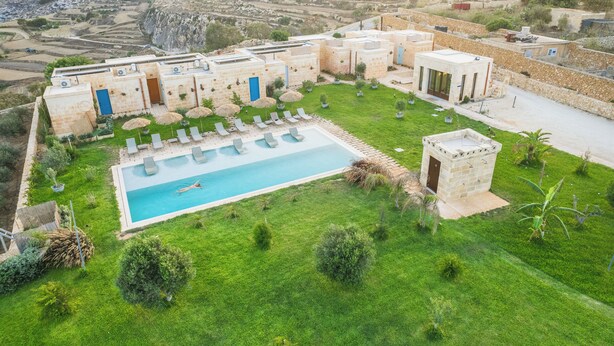Un área de piscina con sillas de descanso y una piscina rodeada de un césped cuidado y edificios de piedra.