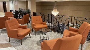 A lobby with orange armchairs arranged around a central area, a chandelier, and a railing with a decorative plant. - Putra Brasmana Hotel (Kuala Perlis)