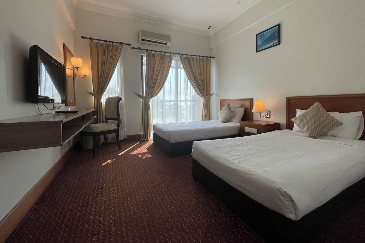 A hotel room with two beds, a desk with a chair, a television, and a window with curtains.
