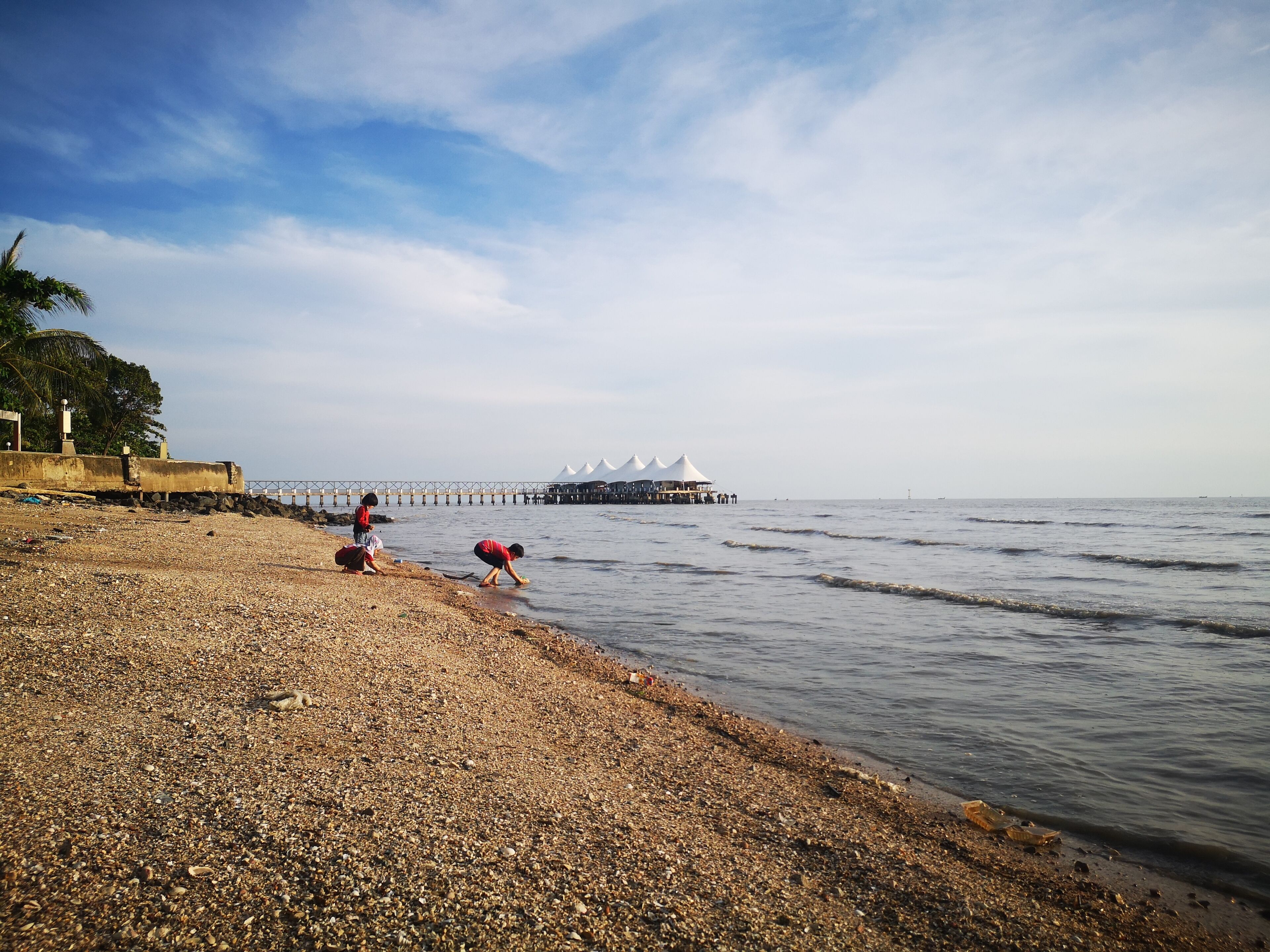 A pebbled beach with a pier extending into the water, featuring white tents.
