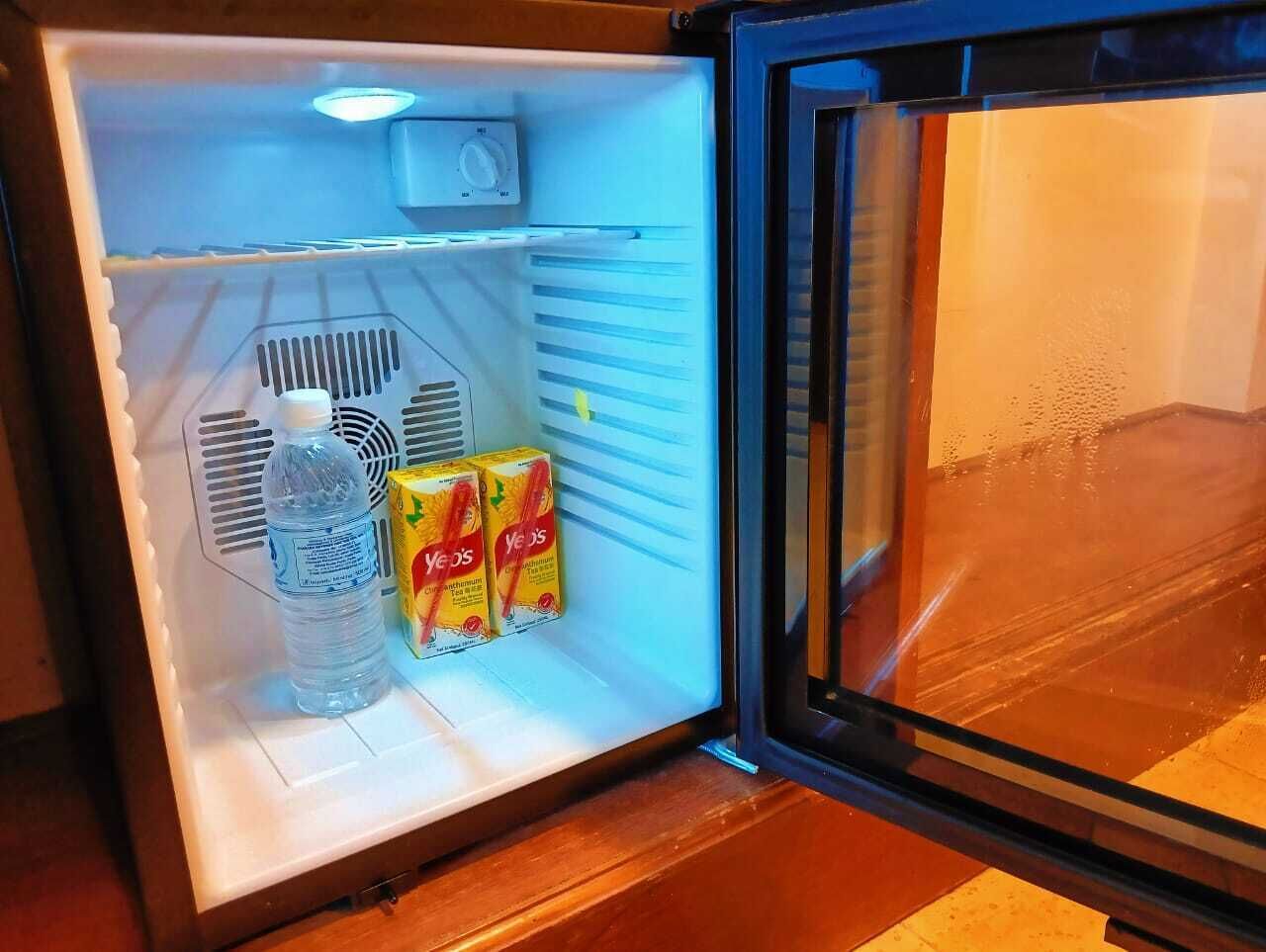 Un réfrigérateur ouvert, avec une bouteille d’eau et deux briques de jus d’orange de la marque Yeo’s.