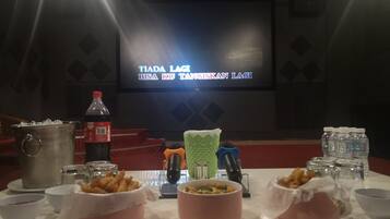 A dining table with food and drinks, a projector screen in the background, and a stage with a red carpet.