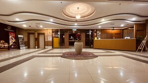 A spacious lobby with a central decorative vase, a reception desk, and a clear path leading to the elevators. - Putra Brasmana Hotel (Kuala Perlis)