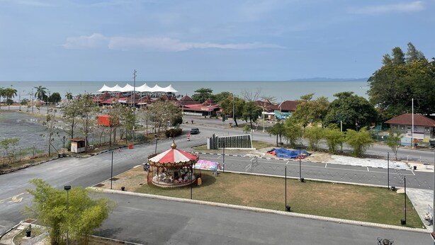 A coastal area with a carousel, open-air restaurants, and a road leading to the beach. - Putra Brasmana Hotel (Kuala Perlis)