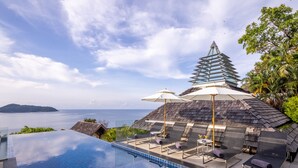 An infinity pool with lounge chairs and umbrellas, overlooking a body of water and a mountainous landscape. - Villa Benyasiri (Kamala)
