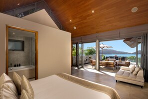 A modern bedroom with a large bed, a bathroom with a bathtub, and a balcony with outdoor furniture overlooking a scenic view. - Villa Benyasiri (Kamala)