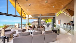 A spacious living area with a large sofa set, a coffee table, and a view of the ocean. - Villa Benyasiri (Kamala)