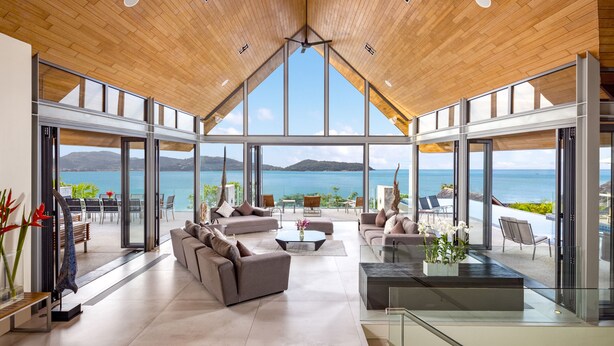 A spacious living area with a high ceiling, large windows, and a view of the sea. - Villa Benyasiri (Kamala)