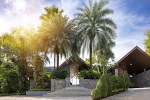 A modern building with a stone facade and a wooden roof, surrounded by lush greenery and palm trees. - Villa Benyasiri (Kamala)