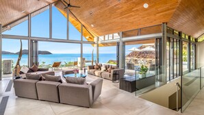 A spacious living area with a large window overlooking the sea, furnished with sofas and a coffee table. - Villa Benyasiri (Kamala)