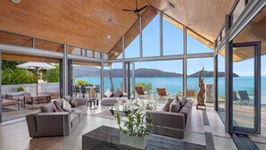 A spacious living area with a large glass wall offering a view of the sea and mountains. - Villa Benyasiri (Kamala)