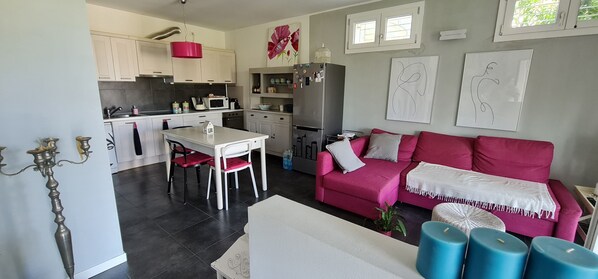 Une cuisine moderne avec des meubles blancs, un luminaire rouge suspendu et un coin repas comprenant une table blanche et des chaises rouges.