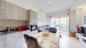 Een compact appartement met kitchenette, een eethoek met tafel en stoelen, een bank en een balkon met televisie.
